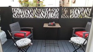 Un patio con dos sillas y una mesa pequeña, una cerca decorativa y vistas de edificios al fondo.