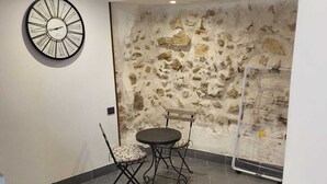 Una habitación con pared de piedra, una mesa redonda con sillas, un reloj en la pared y una barrera de plástico transparente.