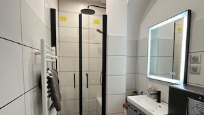 Un baño moderno con cabina de ducha de vidrio, un lavamanos blanco y un espejo grande.