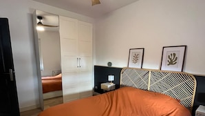 Un dormitorio con cama, ventilador de techo, mesita de noche y estante en la pared.