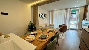 Un espace repas moderne avec une table en bois disposée pour quatre personnes, entourée de chaises à l’assise rembourrée de tissu vert.