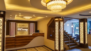 A reception area with a reception desk, a chandelier, and a staircase leading to a dining area. - Kathmandu Royal Chamber Hotel (Kathmandu)