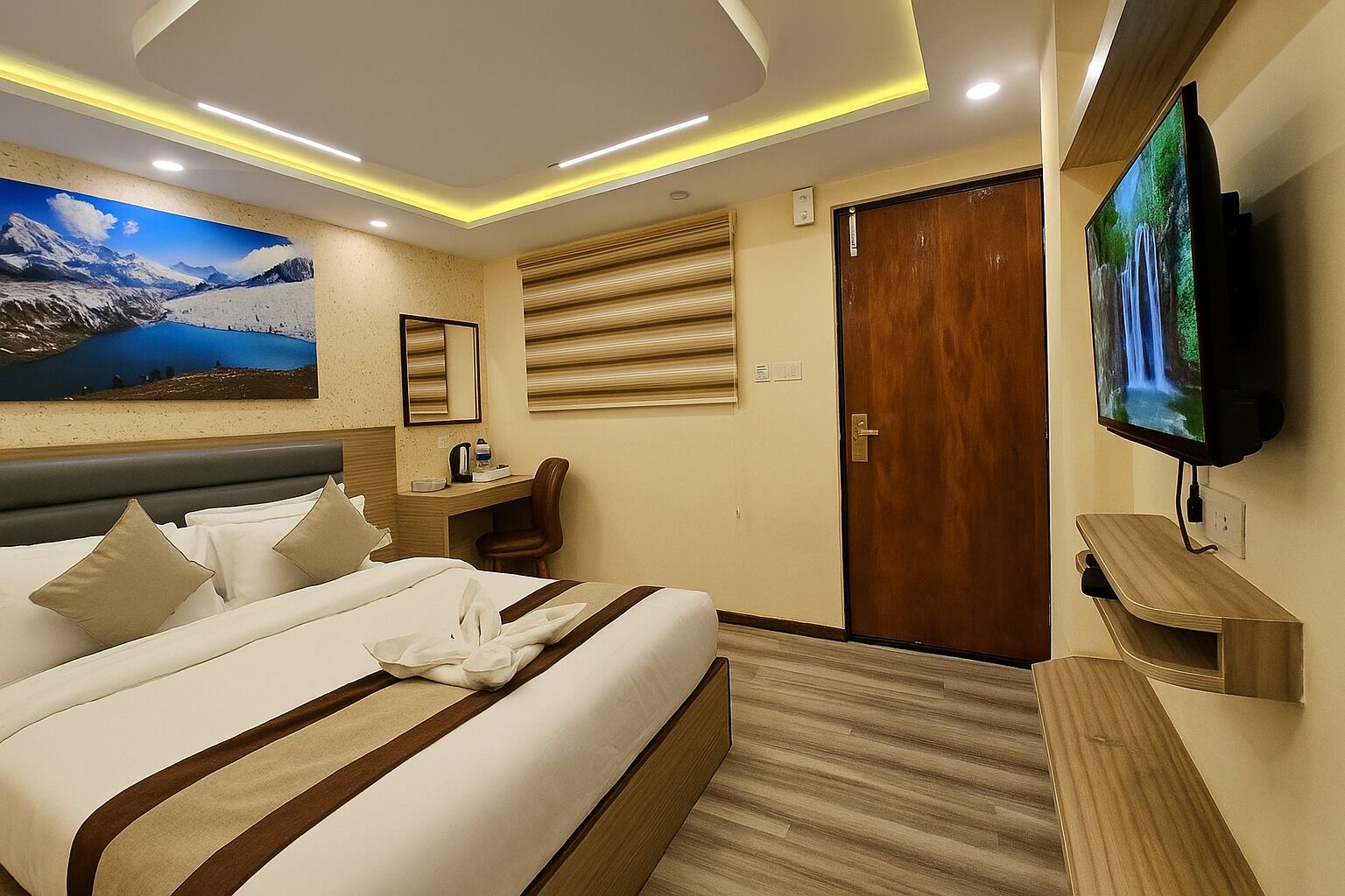 A hotel room with a large bed, a desk, a television, and a painting of a mountain landscape.