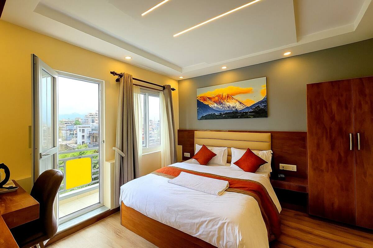 A hotel room with a bed, a desk, a chair, a wardrobe, and a painting on the wall.