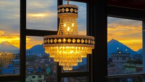 A chandelier with a reflective surface and a geometric design, hanging in front of a window with a view of a mountain and buildings. - Kathmandu Royal Chamber Hotel (Kathmandu)
