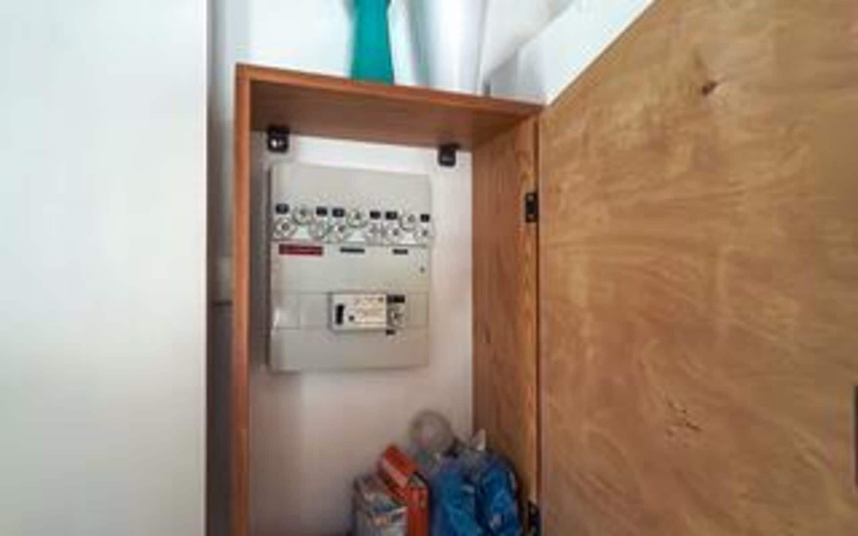 Una sala de servicios con un cuadro eléctrico, una puerta de madera y algunos objetos en el suelo.