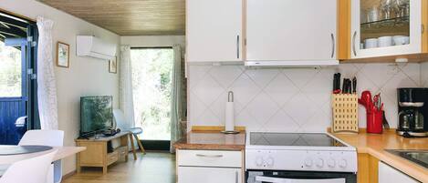 Een compacte keuken met witte kasten, een fornuis, oven en een eethoek met een tafel en stoelen.