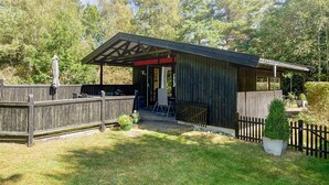 A wooden cabin with a covered patio, surrounded by a wooden fence and a small garden. - 6 Person Holiday Home in Hojby (Hojby)
