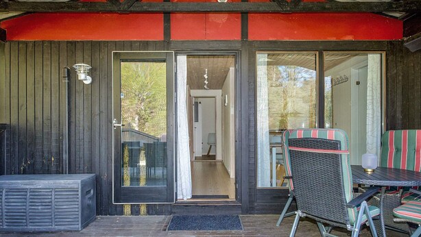 A covered outdoor area with a wooden deck, a glass door leading inside, and outdoor furniture. - 6 Person Holiday Home in Hojby (Hojby)
