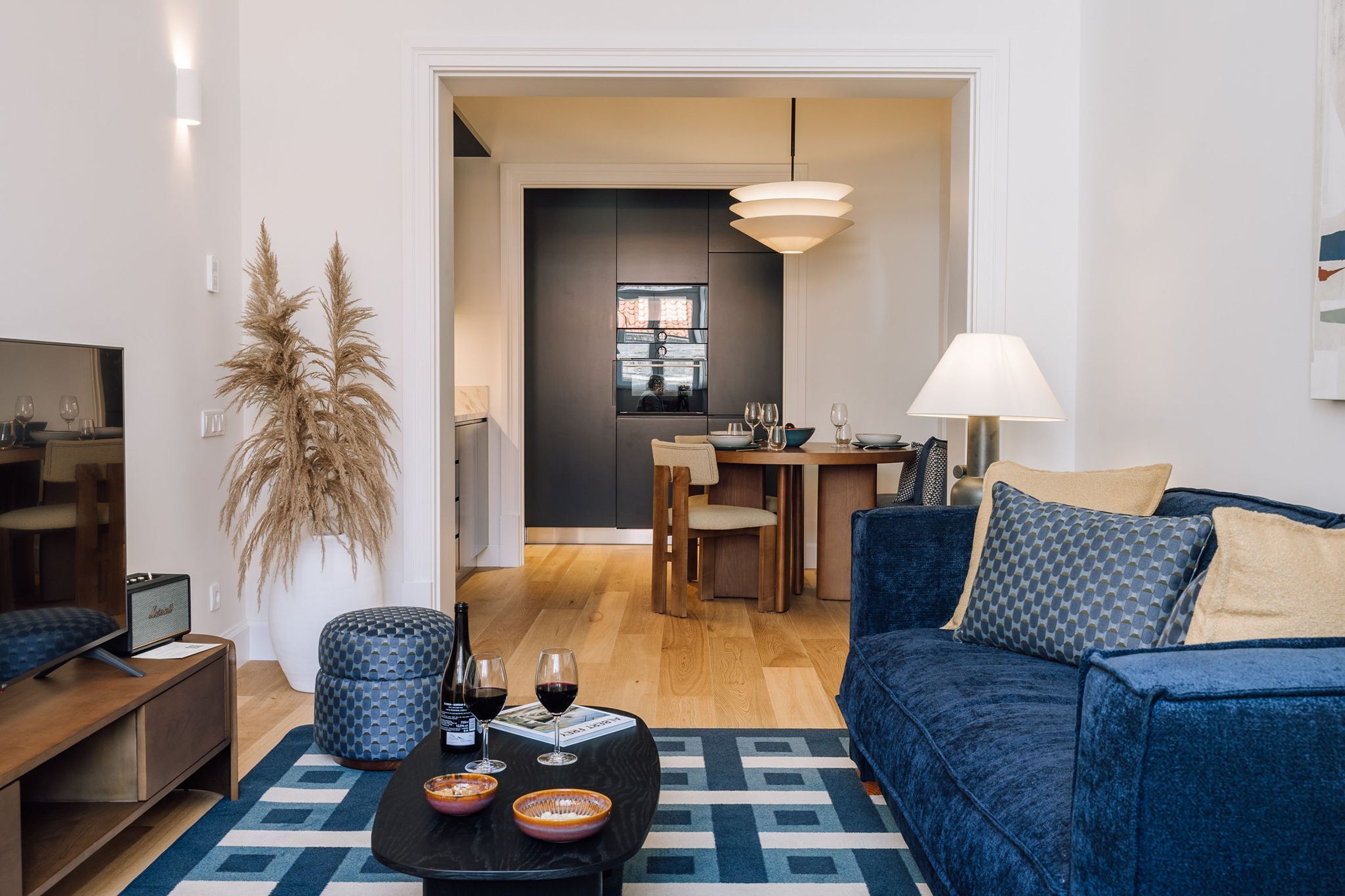 Un salon moderne avec un canapé bleu foncé, une table basse sur laquelle sont posés des verres à vin, un téléviseur et une grande plante en pot.