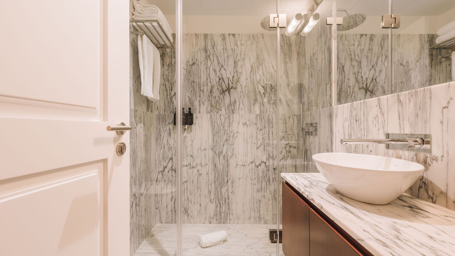 A bathroom with a large marble sink, a glass shower enclosure, and a marble-tiled wall.