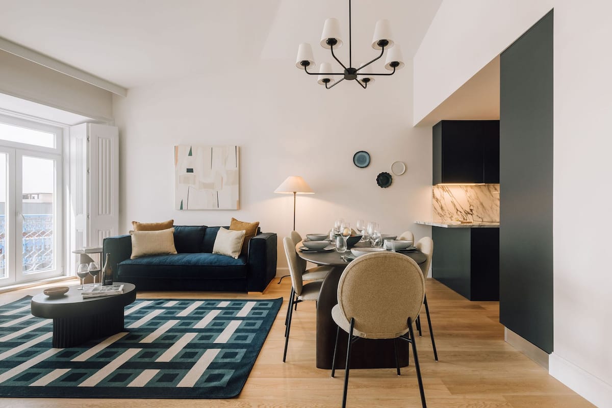 A modern living room with a dark blue sofa, a round coffee table, a patterned rug, and a dining area with a table set for four.