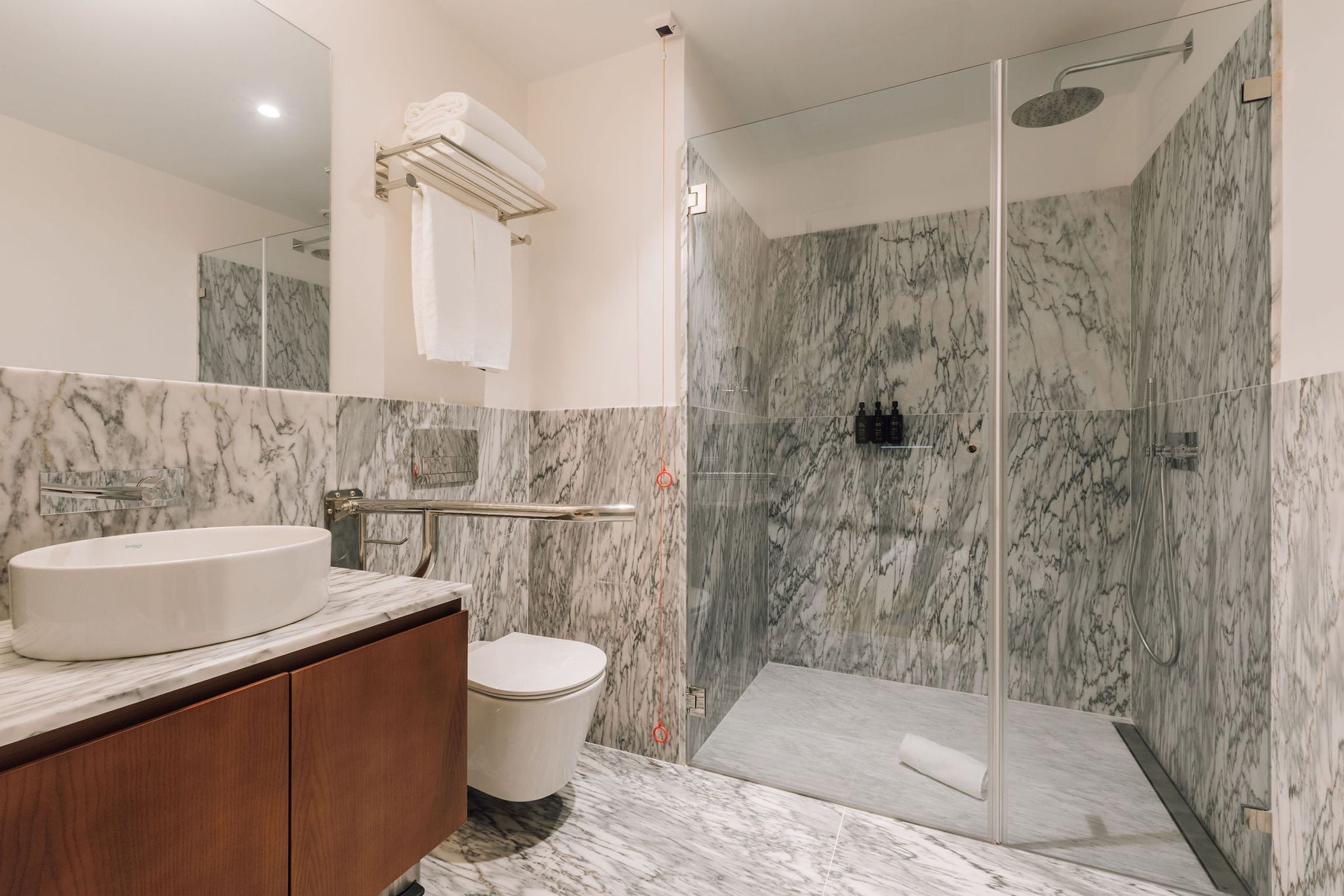 A modern bathroom with a marble vanity, a toilet, and a glass-enclosed shower area.