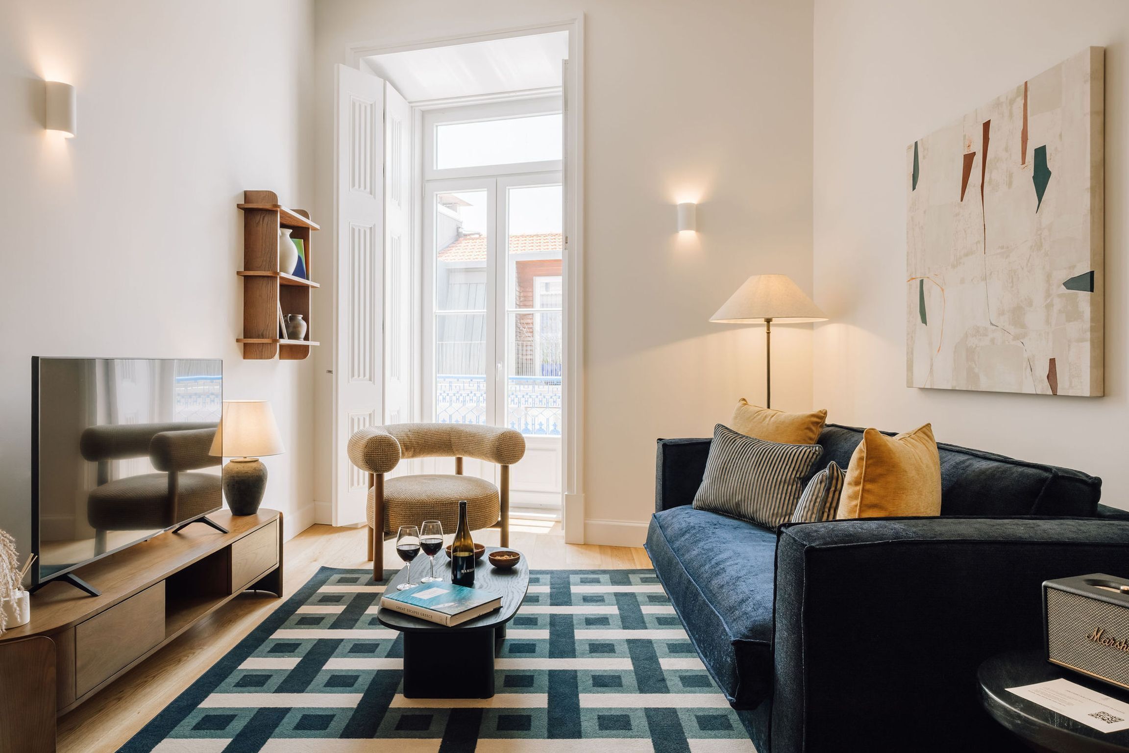 Un salon moderne avec un canapé, un téléviseur et une table basse. On y trouve également une bibliothèque, une lampe et un tableau accroché au mur.