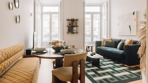 A modern living room with a dining table, sofa, and a green patterned rug. - Ando Living - Abrantes 50 House (Lisbon)
