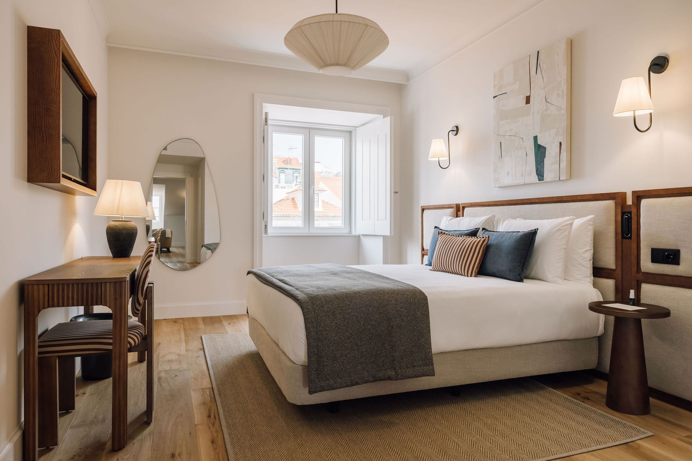 Un dormitorio con cama, mesita de noche, lámpara, silla y vistas al exterior.
