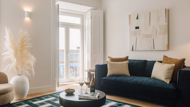 A modern living room with a dark blue sofa, a round coffee table, and a large window with a view of a balcony. - Ando Living - Abrantes 50 House (Lisbon)