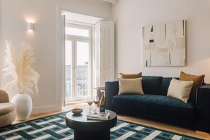 Una sala moderna con un sofá azul oscuro, una mesa redonda de centro y un ventanal con vistas a un balcón.