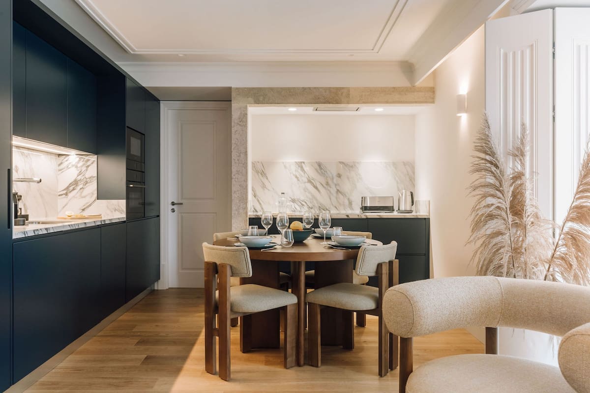A modern kitchen with dark cabinetry, a marble backsplash, and a dining area with a round table and chairs.