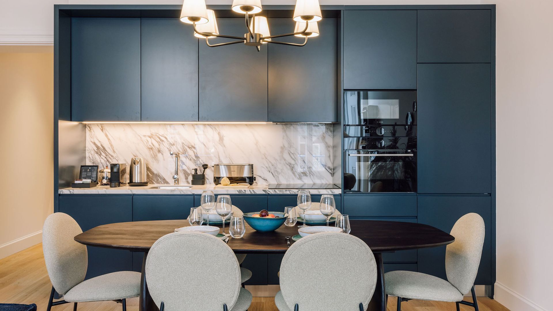 A modern kitchen with dark cabinetry, a marble backsplash, and a built-in oven.