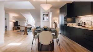 A modern kitchen with dark cabinets, a marble countertop, and a dining area with a round table and chairs. - Ando Living - Abrantes 50 House (Lisbon)