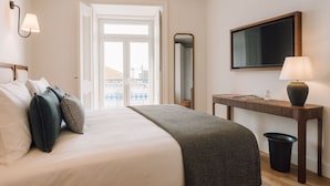 A hotel room with a bed, bedside table, lamp, and a large window with a view of buildings. - Ando Living - Abrantes 50 House (Lisbon)