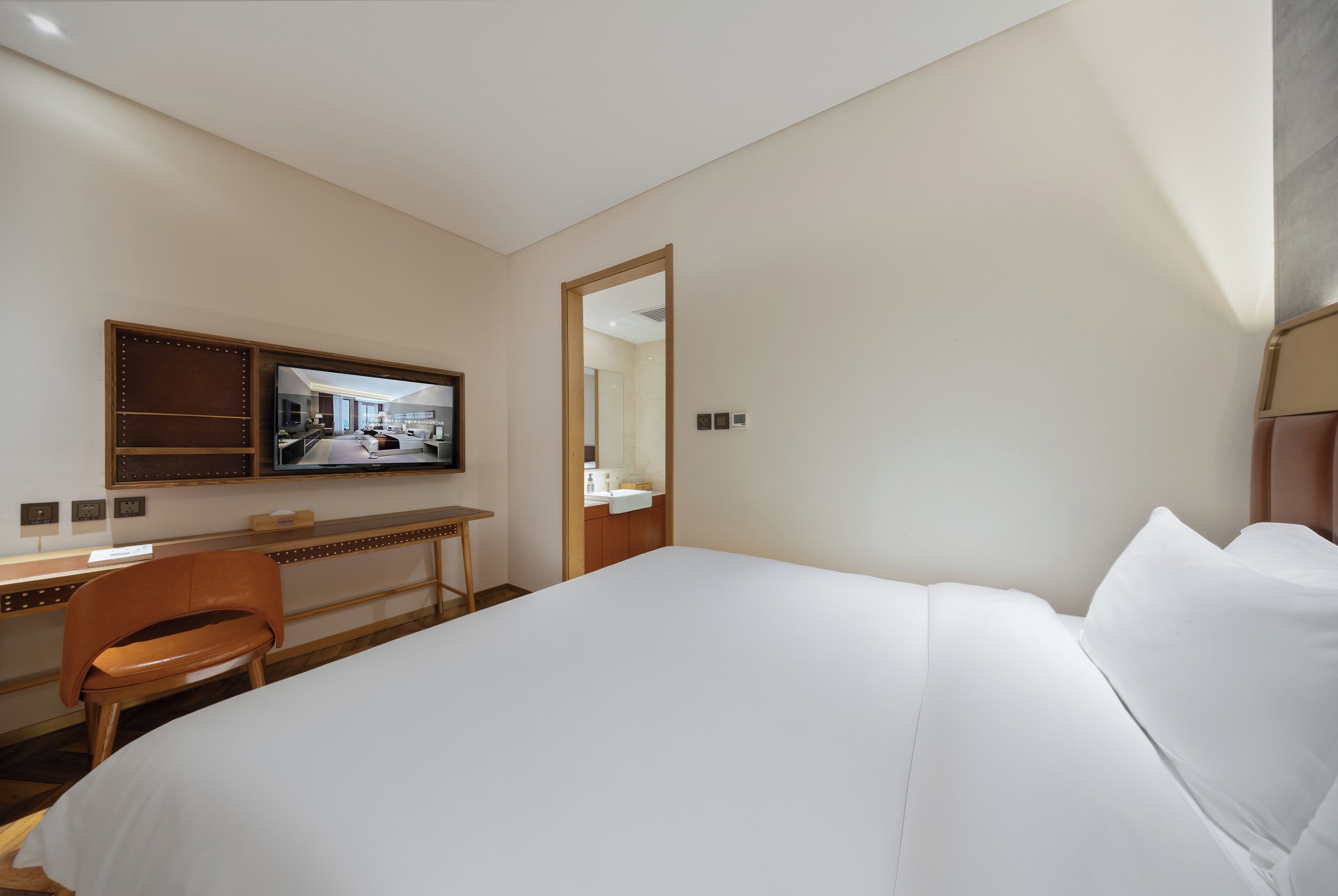 Quarto de hotel com uma cama grande, uma escrivaninha com cadeira, uma televisão e um espelho.