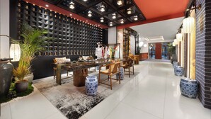 A modern interior with a dining area featuring a long table and chairs, a black wall with a grid pattern, and decorative lighting. - Beijing TangFu Chinese Culture Boutique Hotel Sanlitun Embassy Area (Beijing)