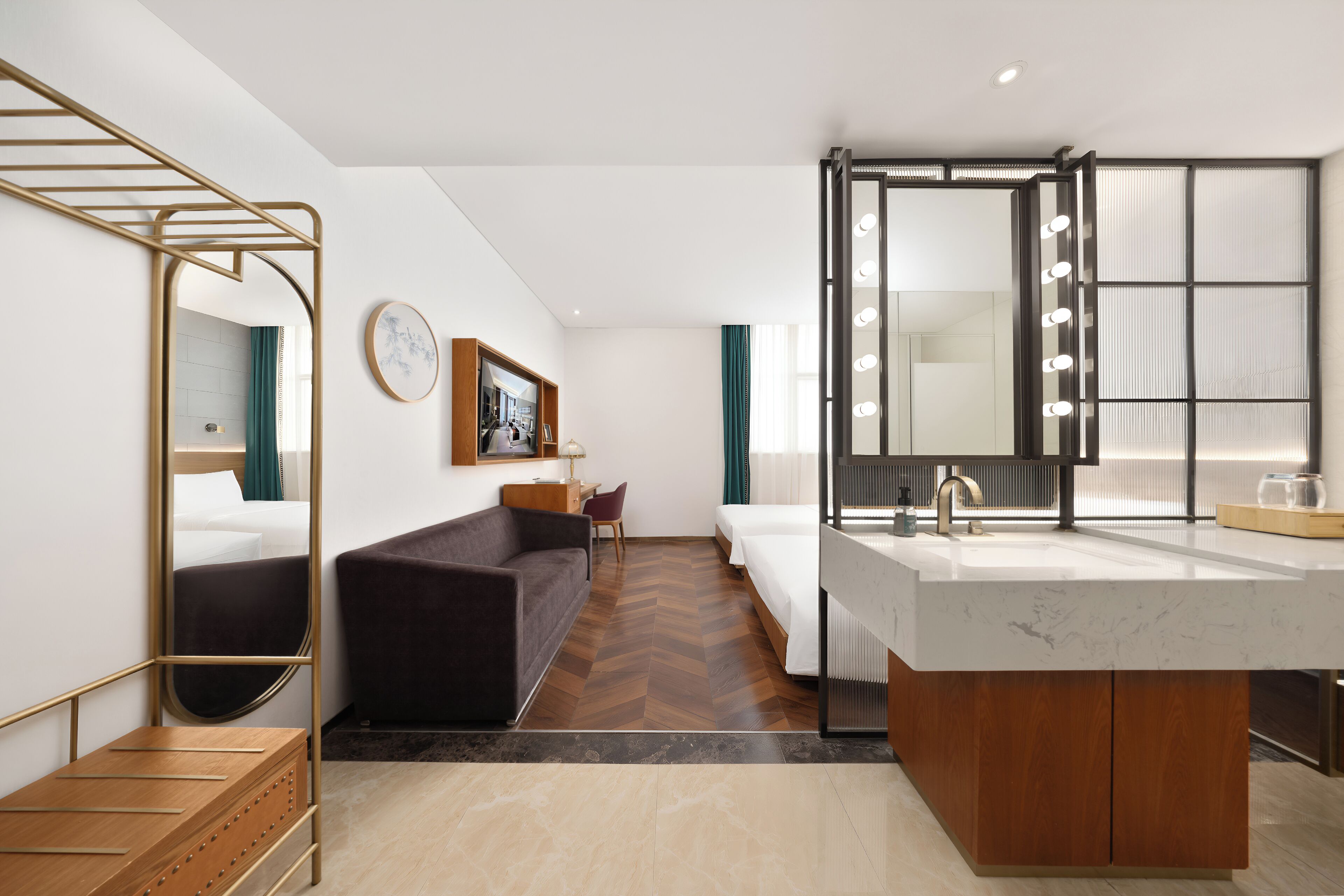 A hotel room with a bed, a sofa, a vanity with a mirror, and a wooden bench.