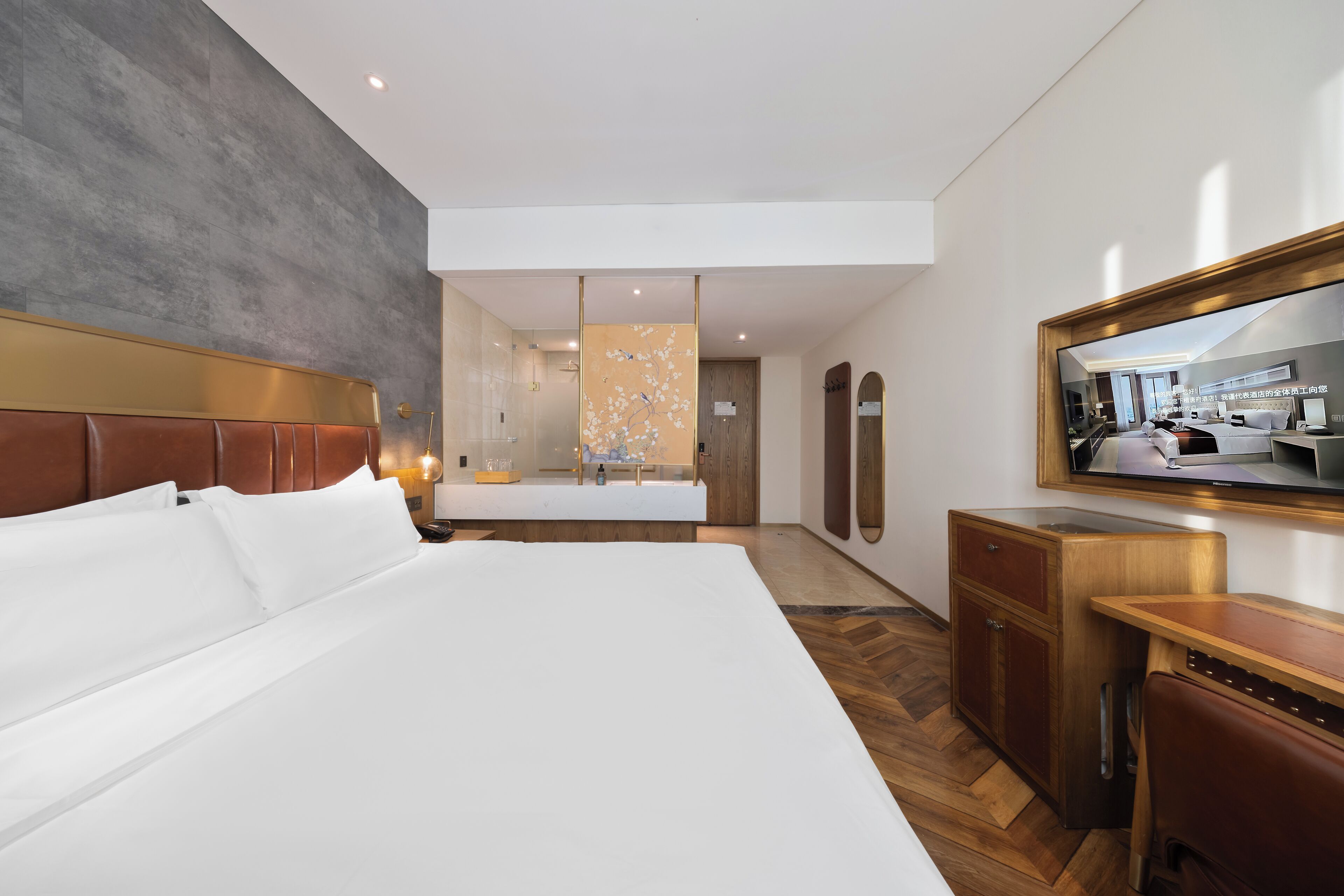 A modern hotel room with a large bed, a wooden desk, a vanity with a mirror, and a view of the bathroom.