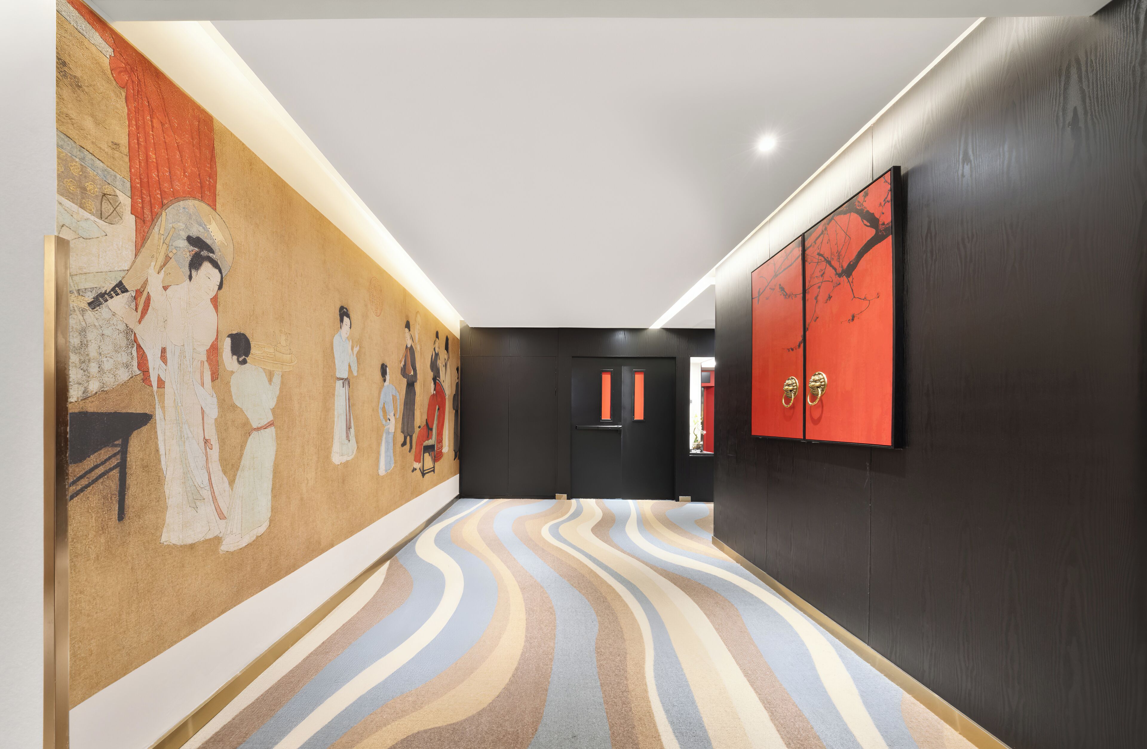 A hallway with a patterned carpet, a mural on the left wall, and a red door with two cabinets on the right.
