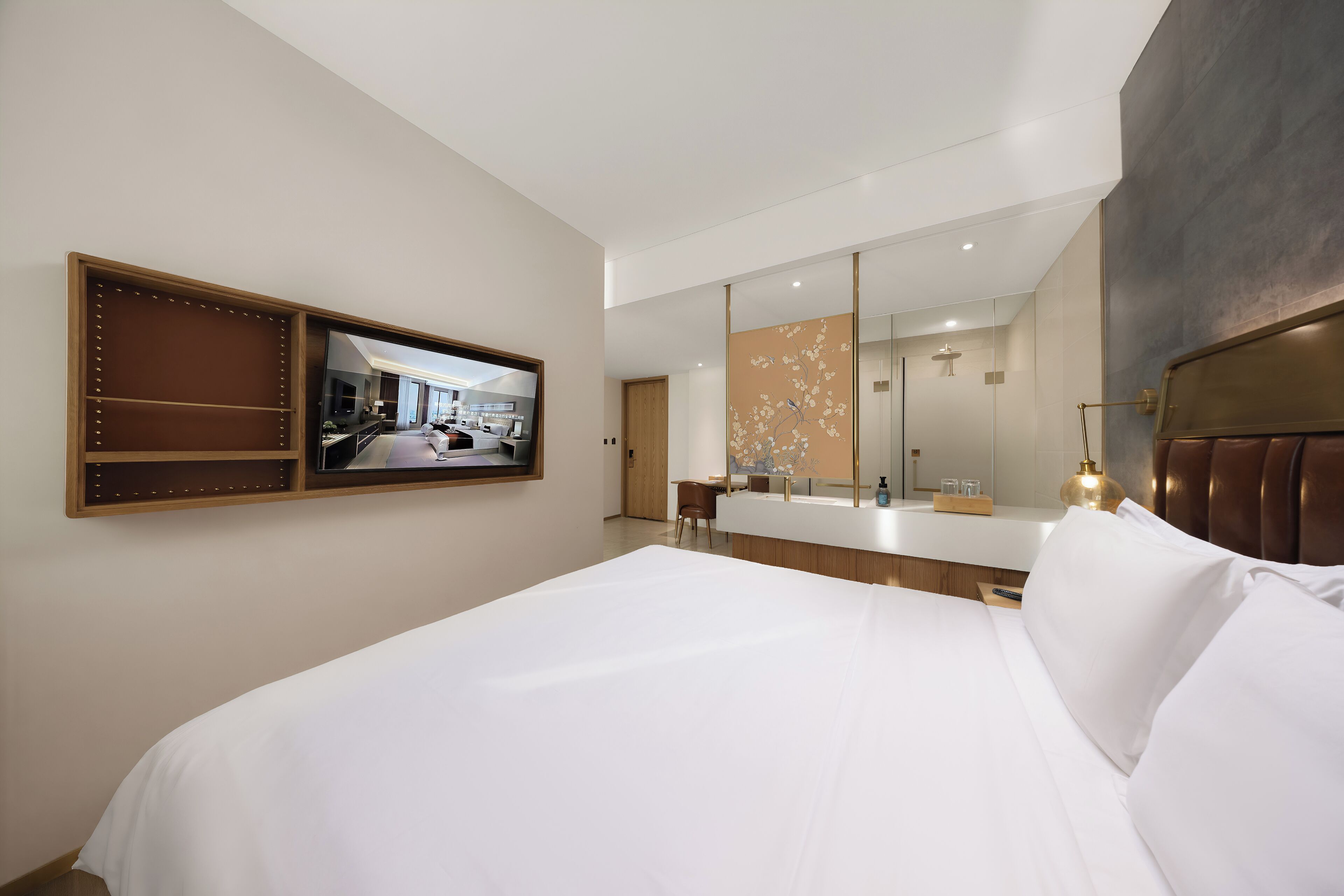 A modern hotel room with a large bed, a built-in TV, a bathroom with a large mirror, and a seating area with a view of the room.