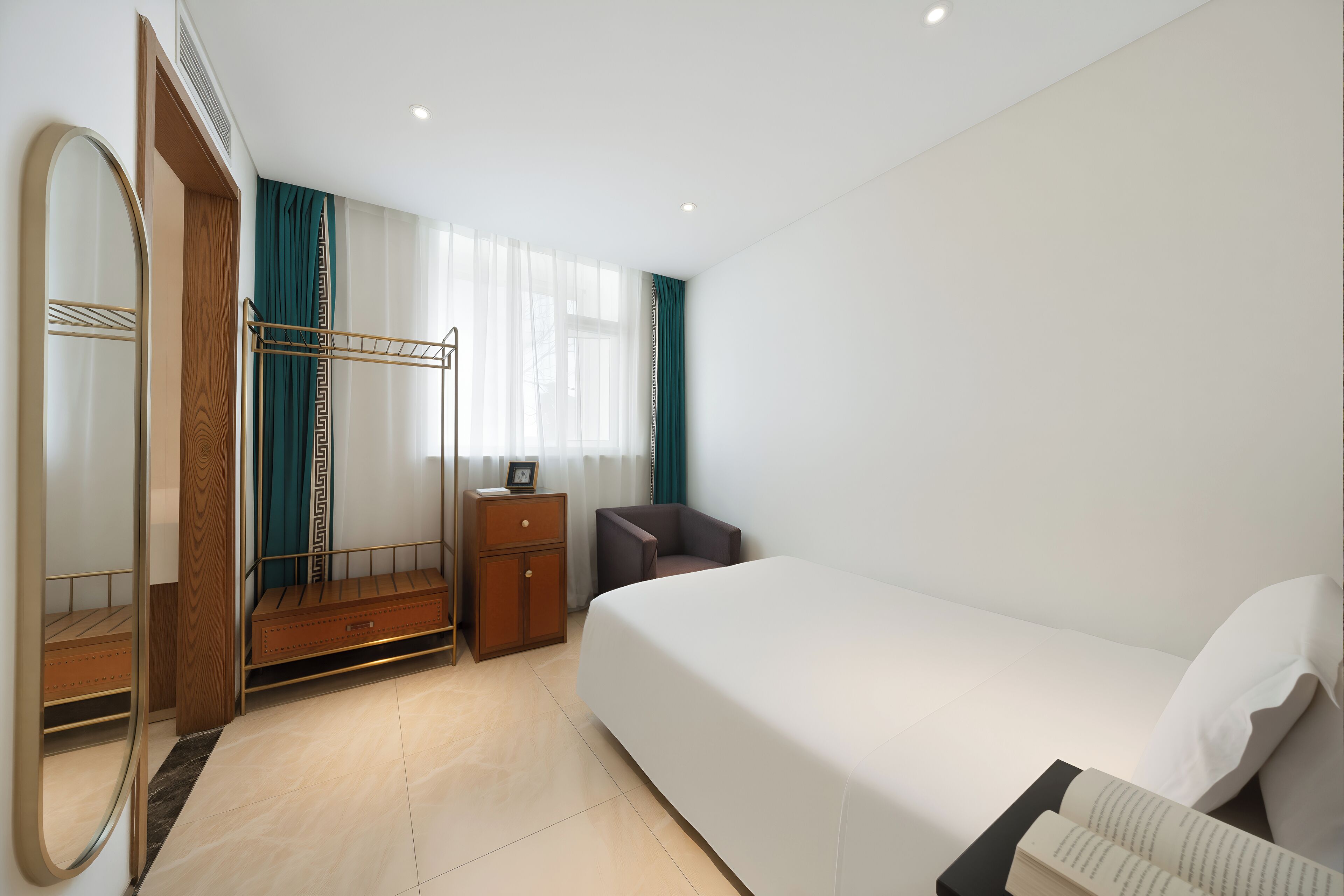 A hotel room with a bed, a wardrobe, a mirror, a bedside table, and a window with curtains.