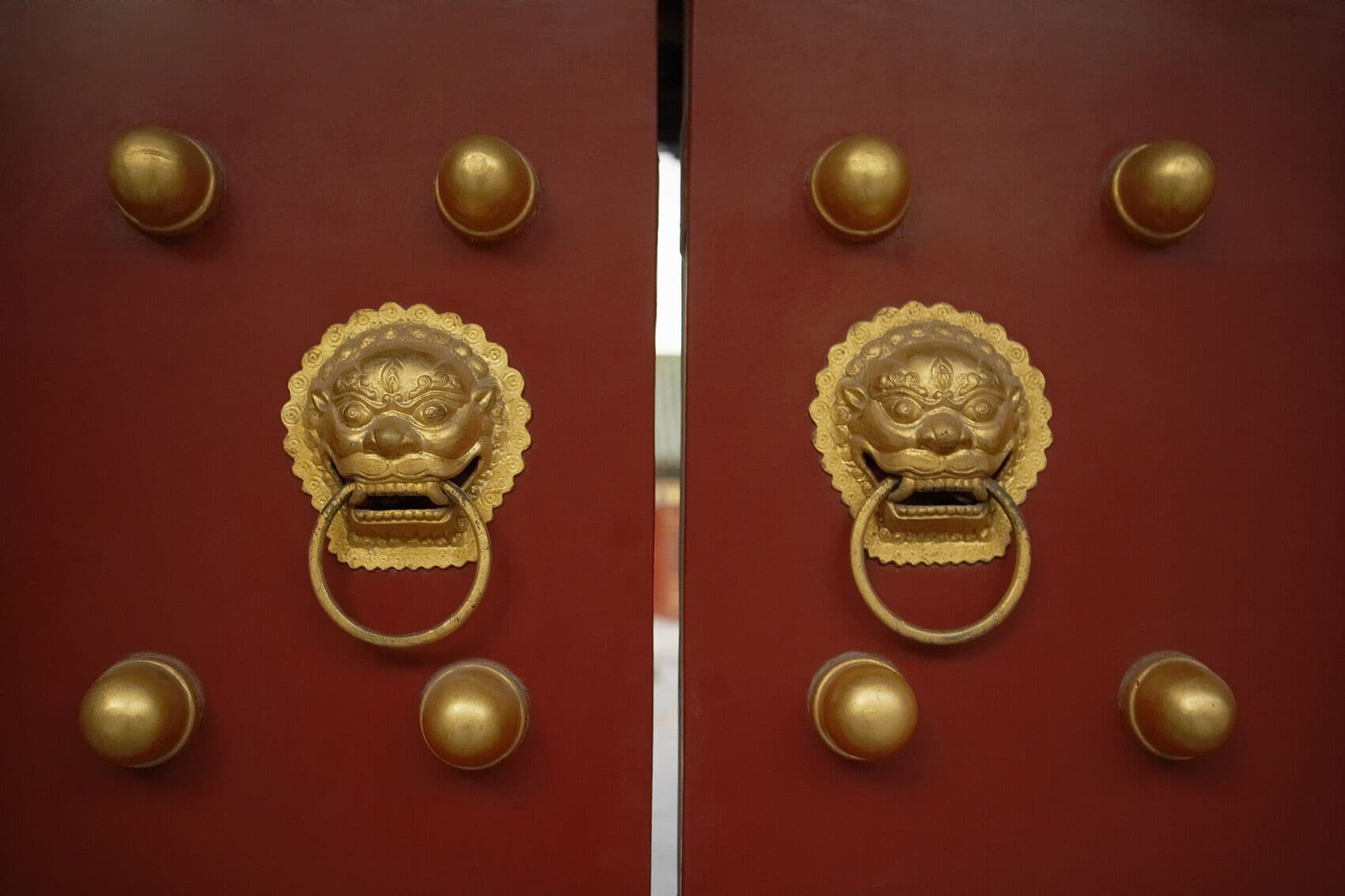 A pair of red doors with gold handles and decorative lion heads.