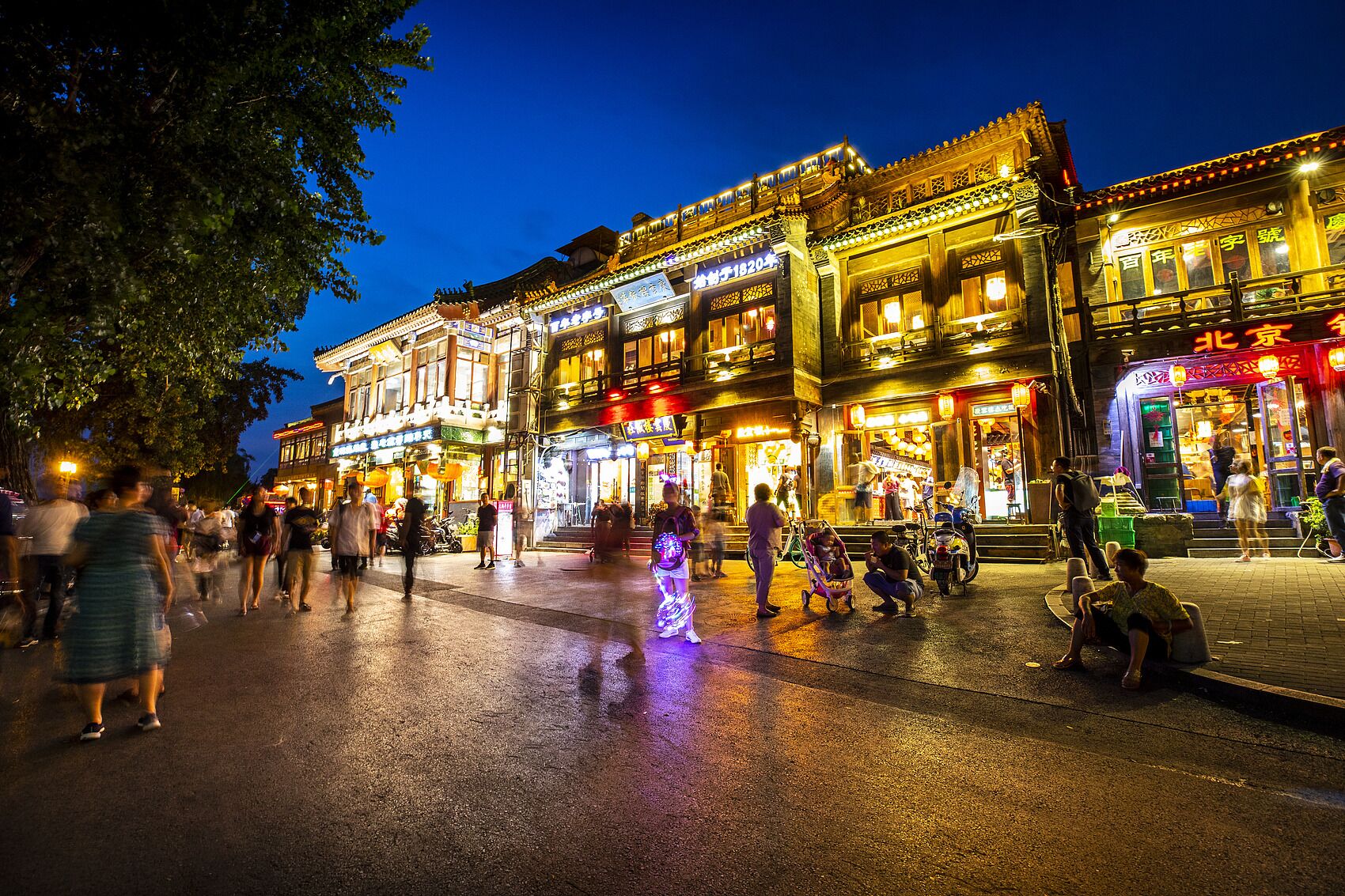 Une rue historique aux bâtiments d’architecture traditionnelle, un pavé mouillé et des passants.