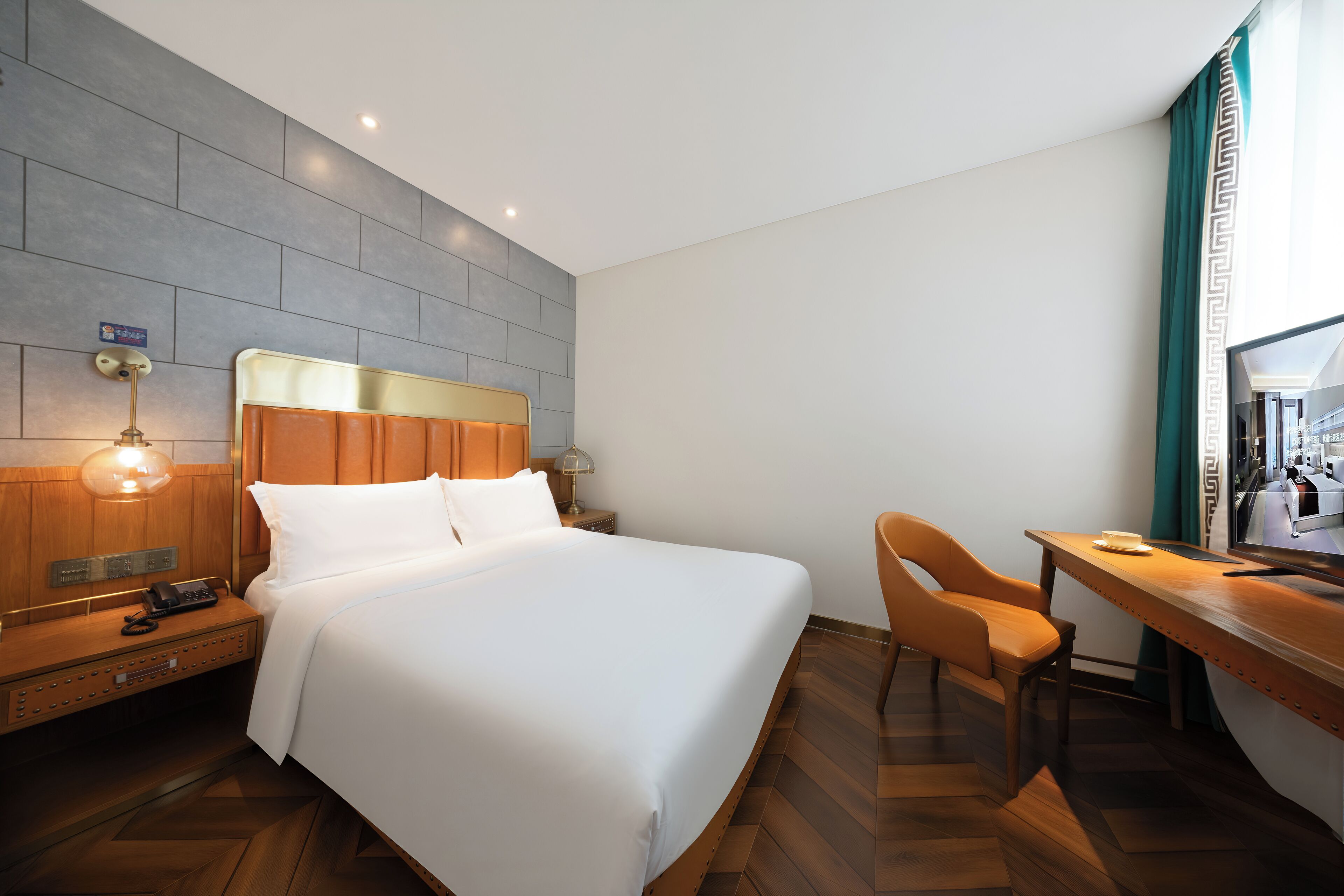 A hotel room with a large bed, a desk, and a chair. There is a nightstand with a lamp and a phone. The room has a modern design with a herringbone floor pattern.