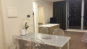 A modern living room with a dining area, a kitchen in the background, and a large window with a city view. - Central Lakeview Apartments (Canberra)