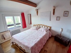 A bedroom with a wooden bed, a window with red curtains, and a wall-mounted lamp. - Spacious villa with pool and views of the sea and garrigue (Frontignan)