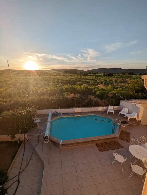 A rectangular swimming pool with a tiled deck, surrounded by white outdoor furniture, and a view of a hilly landscape during sunset. - Spacious villa with pool and views of the sea and garrigue (Frontignan)