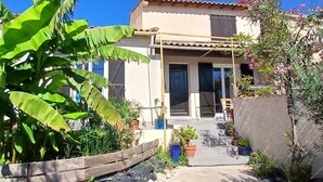 Une maison avec une véranda en bois, des plantes en pot et un grand bananier.