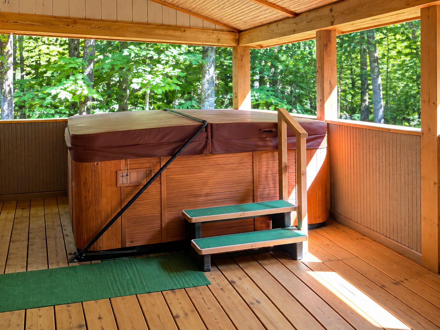 Un jacuzzi con escalones y una terraza de madera, rodeado por una valla de madera y árboles.