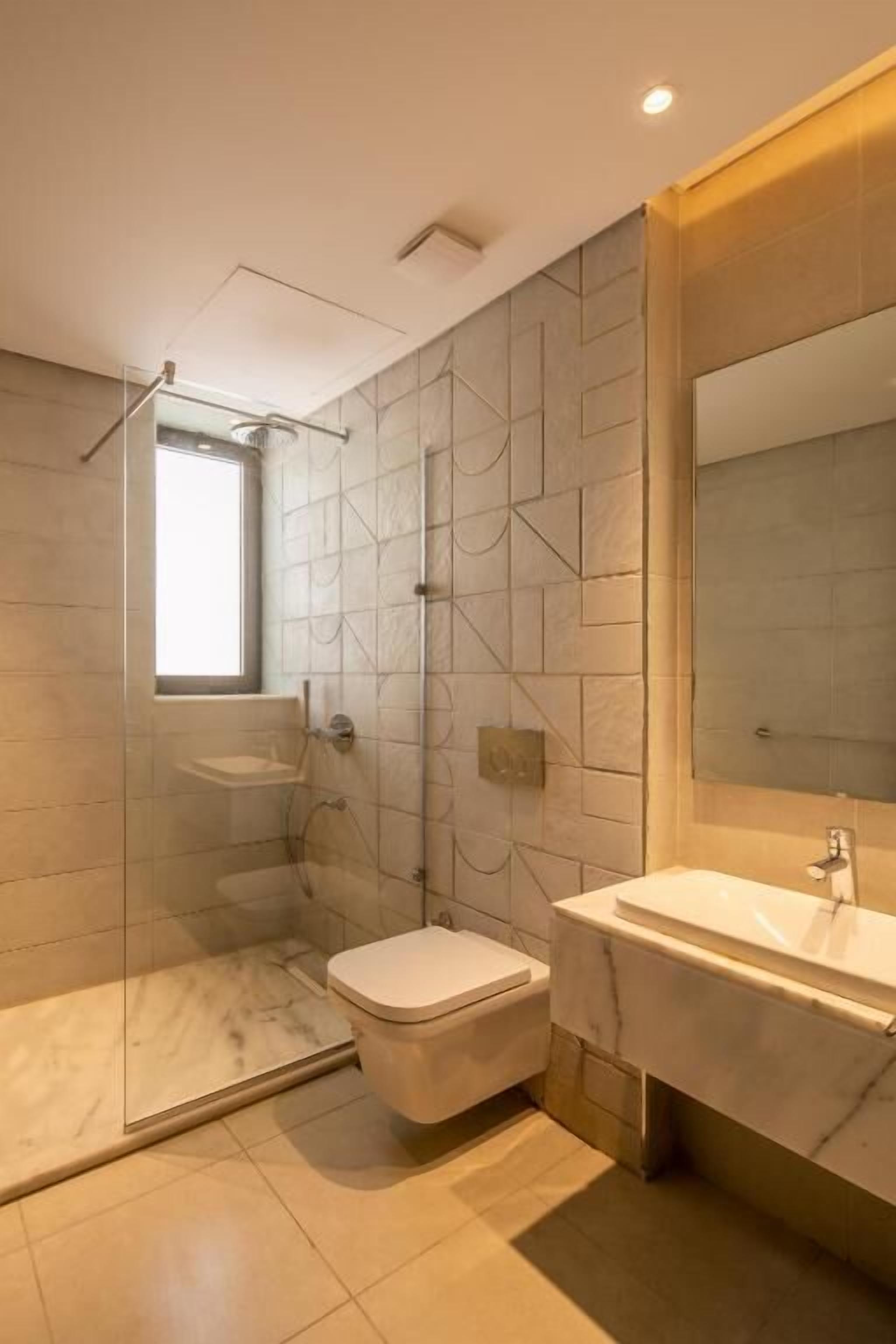Un baño moderno con ducha de vidrio, inodoro y lavamanos con un espejo grande.