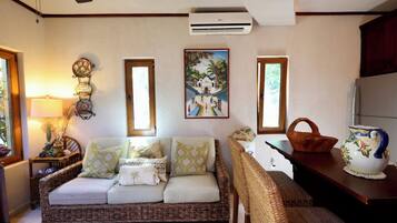 Un salón acogedor con un sofá de mimbre, una mesita con una cesta, una lámpara decorativa y un aire acondicionado instalado en la pared.