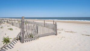 A sandy beach with a wooden fence and sparse vegetation.