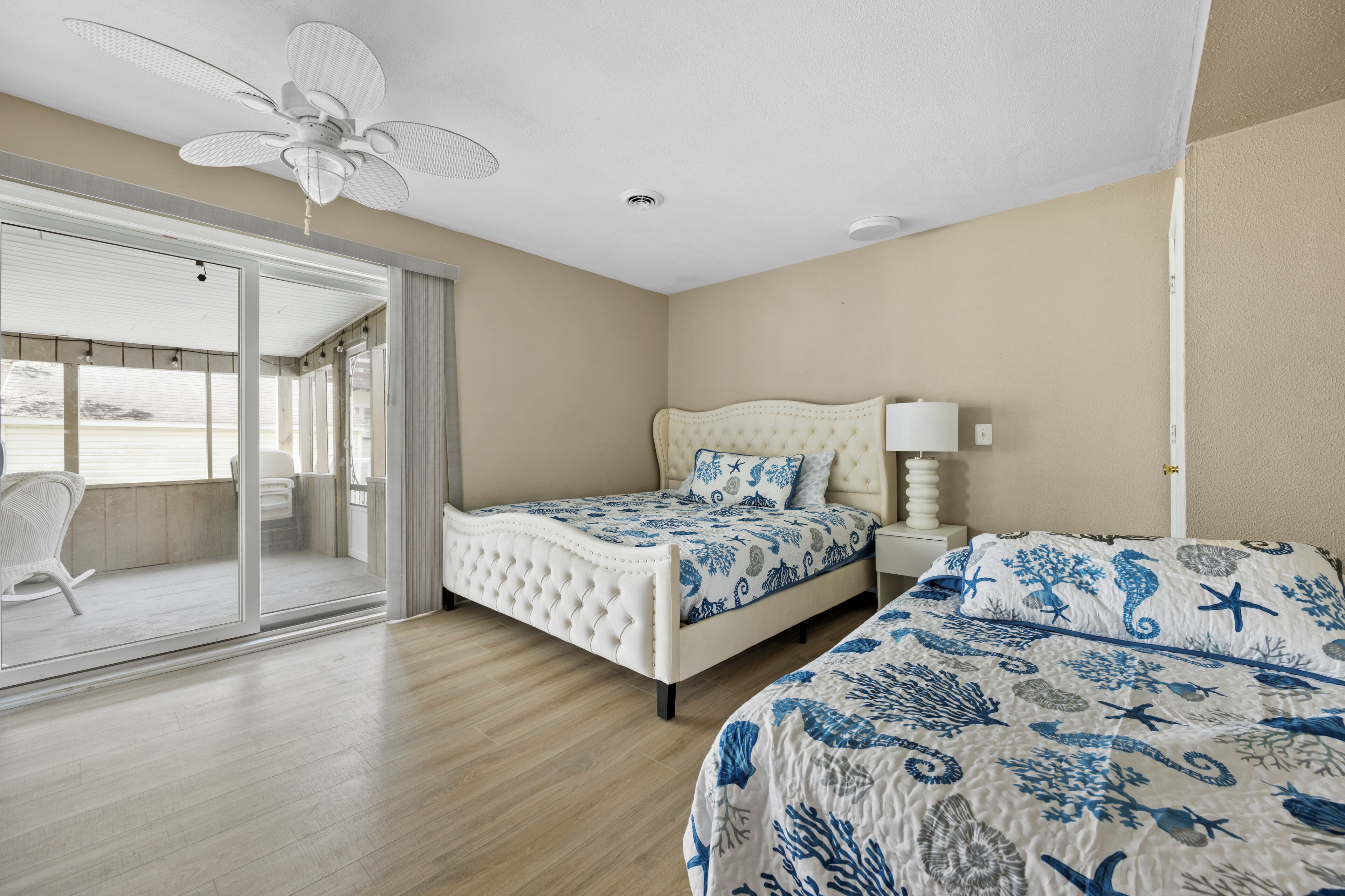 A bedroom with a bed, a nightstand, a ceiling fan, and a sliding glass door leading to a balcony.
