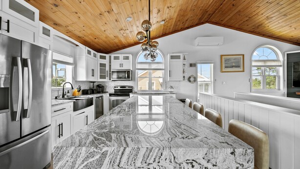 A spacious kitchen with a large island, wooden ceiling, and white cabinetry.