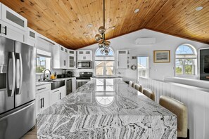 A spacious kitchen with a large island, wooden ceiling, and white cabinetry.