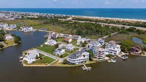 An aerial view of a waterfront residential area with houses, docks, and a beach in the background.
