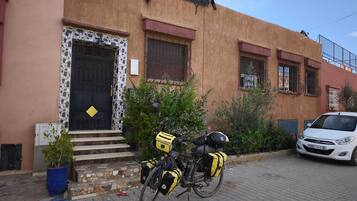 A building with a textured facade, a black door with a yellow diamond-shaped decoration, and a bicycle with yellow and black bags parked in front.