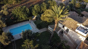 Vista aérea de una propiedad con piscina, un edificio de piedra y vegetación circundante.